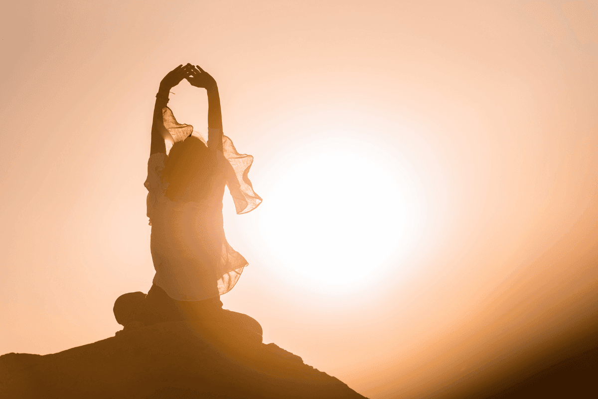 Personne assise, bras levés, silhouette au coucher du soleil.